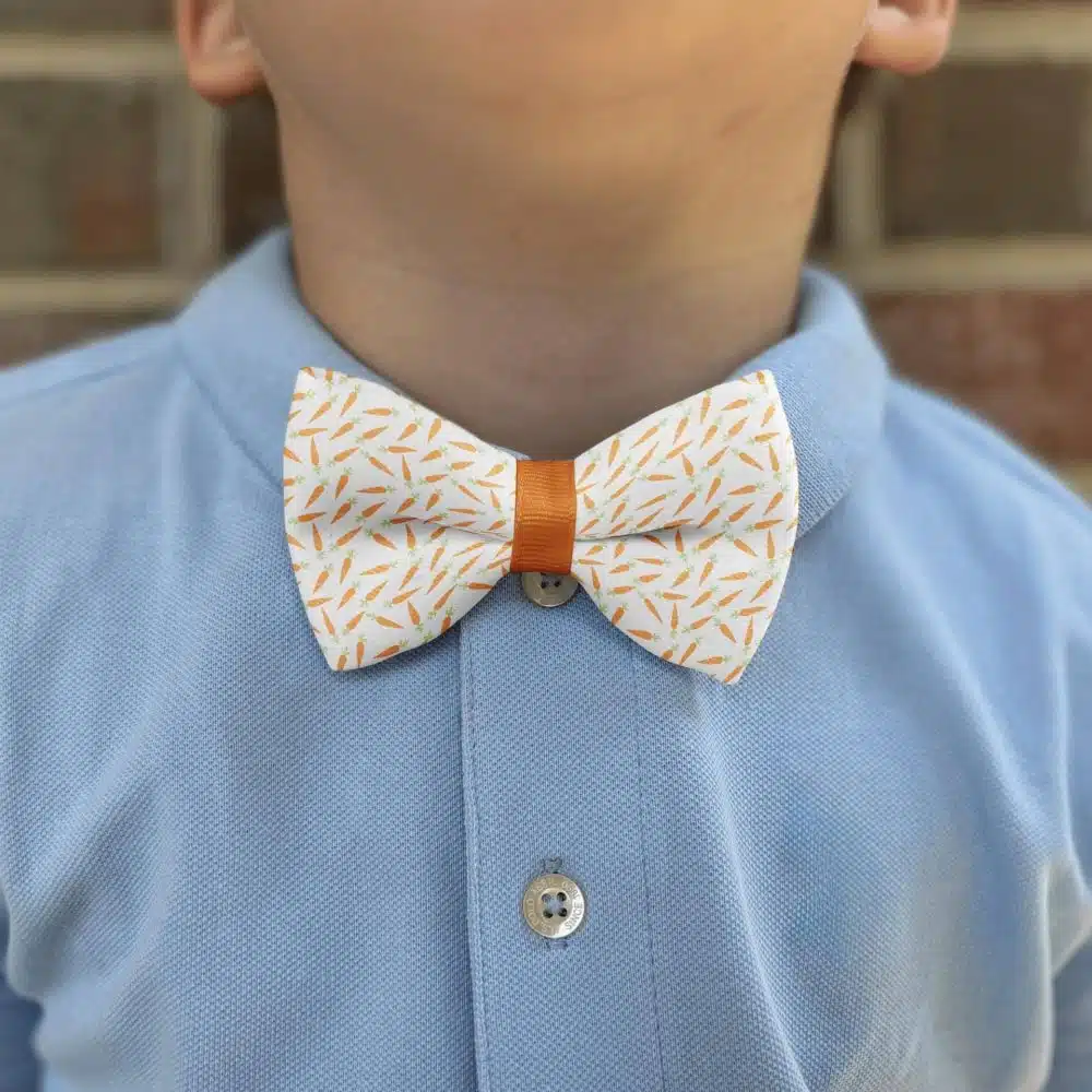 Child wearing carrot-patterned bow tie and blue shirt.