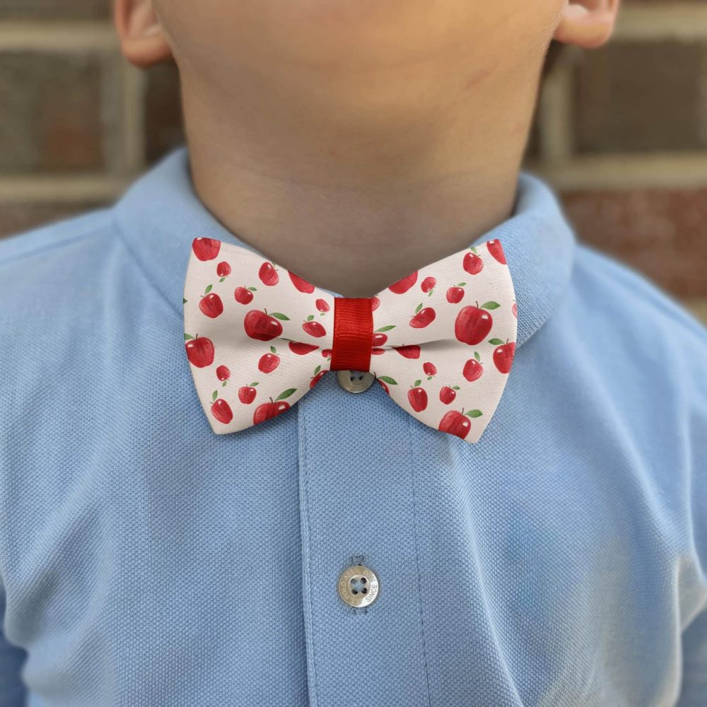 Child wearing apple-patterned bow tie and blue shirt.